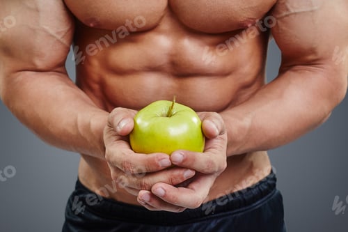 Preview: shirtless bodybuilder holding an apple in his hands.