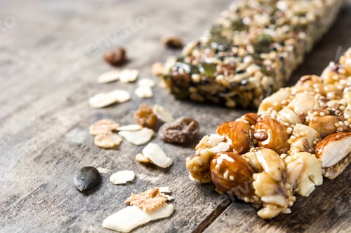 Preview: Two protein bars with nuts, seeds, and dried fruits resting on rustic wooden surface