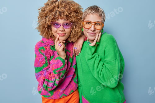 Preview: Photo of pleased lovely women look happily at camera wear sunglasses colorful warm jumpers stand