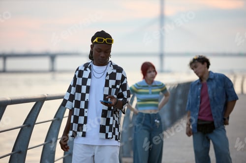 Preview: Teenage Black Boy Using Smartphone While Friends Socializing Outdoors