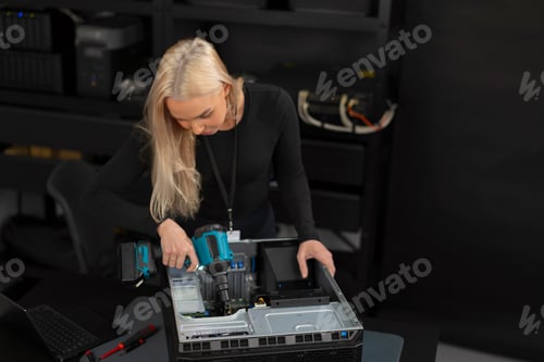 Preview: Female IT technician in her 30s repairs a server inside a computer lab with tools
