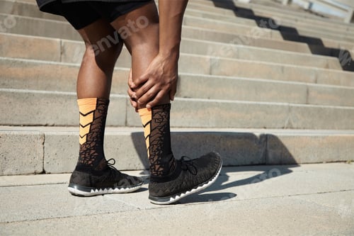 Preview: Sports injury concept. Portrait of young black triathlete runner with cramps in his calf. Young athl