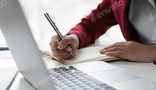 Preview: Professional Business Woman Writing Notes at Desk with Laptop in Modern Office Setting