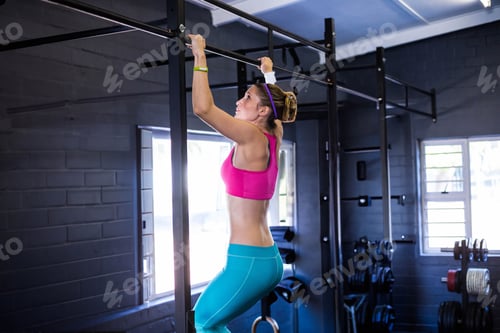 Preview: Adult woman performing pull-up on metal training rig in gym with brick walls, windows, weight racks