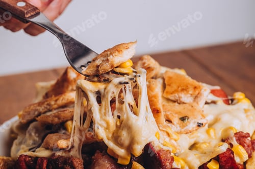 Preview: Closeup shot of a dish with french fries, sausages topped with cheese and corn on a wooden table.