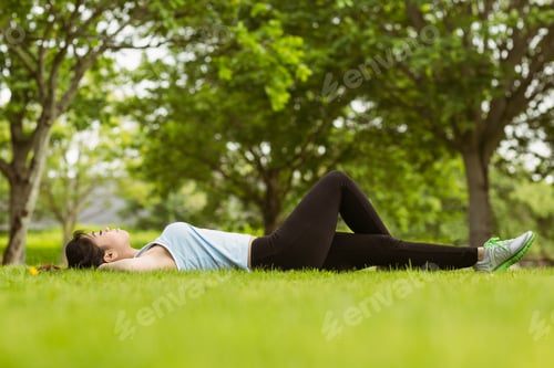 Preview: Side view of healthy and beautiful young woman lying on grass in park