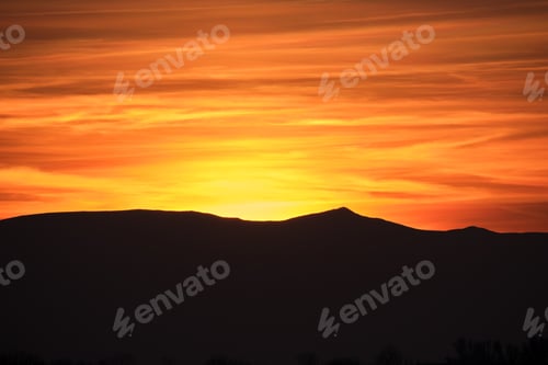 Preview: Beautiful evening panoramic landscape with bright setting sun over distant mountain peaks at sunset