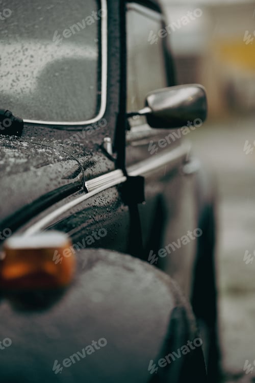 Preview: Vertical closeup of a black car's side part on a rainy day.