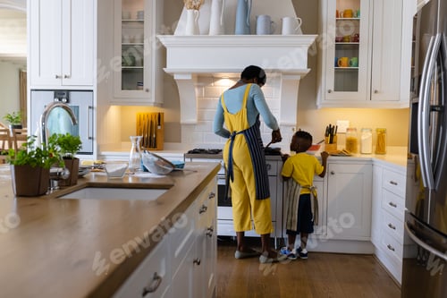 Preview: Rear view of african american mother with son cooking pancakes in kitchen