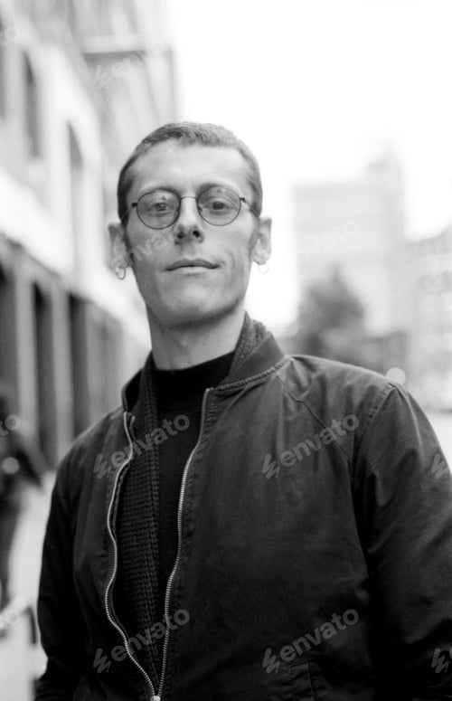 Preview: Young man wearing glasses and jacket posing in urban setting, monochrome analog photography