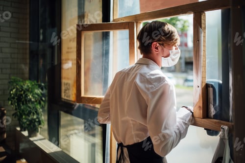 Preview: The masked waiter stands near the takeaway window. Precautions during quarantine in a cafe.