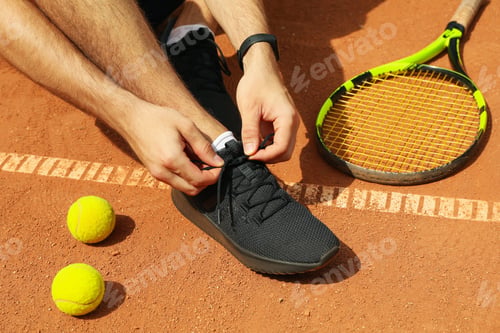 Preview: Man ties his shoelaces on clay court with racket and balls