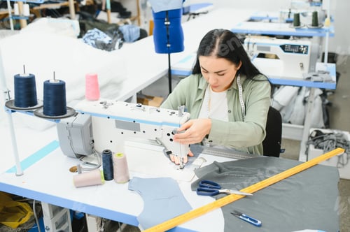 Preview: Young woman working as seamstress in clothing factory.