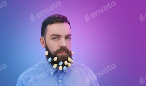 Preview: Portrait of handsome bearded man looking at camera with Easter eggs decoration in beard on violet.