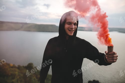 Preview: Ultras hooligan holding red smoke bomb in hand with amazing view on river