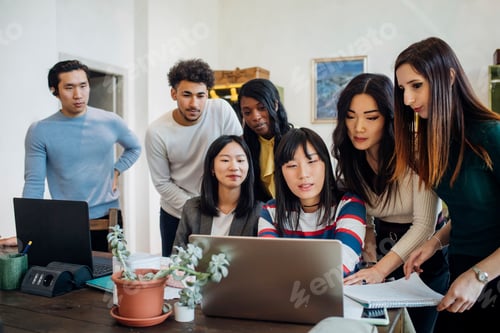 Preview: Group of young businesswomen and men looking at laptop in office meeting