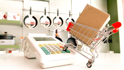 Preview: Mini shopping cart with a box and calculator isolated on a pink surface