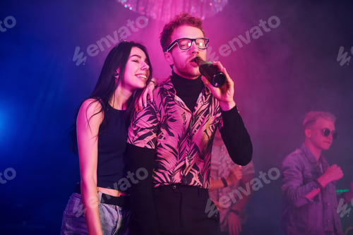 Preview: Guy in glasses drinks beer. Young people is having fun in night club with colorful laser lights