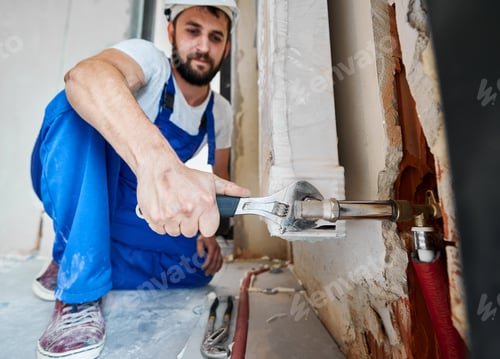 Preview: Male worker installing heating radiator in apartment.