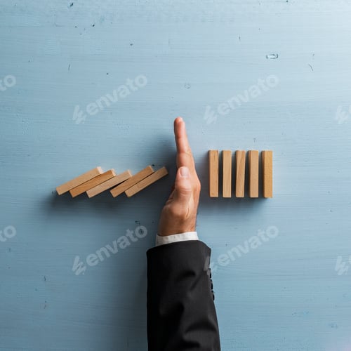 Preview: Overhead view of hand in a business suit stopping or intervening collapsing dominos