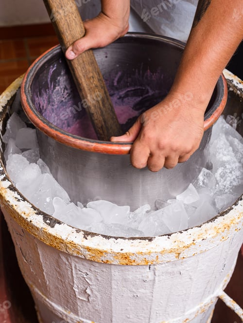 Preview: A person hand-churns purple ice cream in an old-fashioned ice cream maker, surrounded by ice