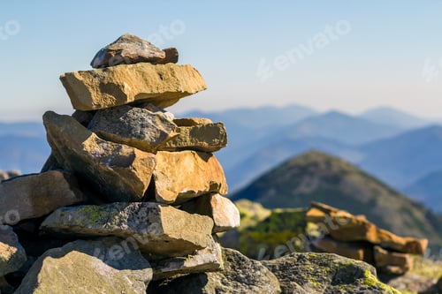 Preview: Stack of stones covered with moss on top of a mountain on mountains background. Concept of balance