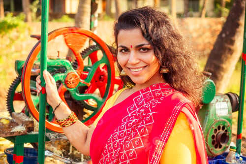 Preview: beautuful induan woman in red sari standing near sugarcane juice maker apparatus machine