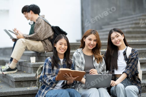 Preview: A group of female students with laptops and books while sit on the steps near the campus or universi