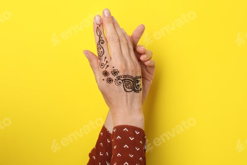 Preview: Woman with henna tattoo on hand against yellow background, closeup. Traditional mehndi ornament