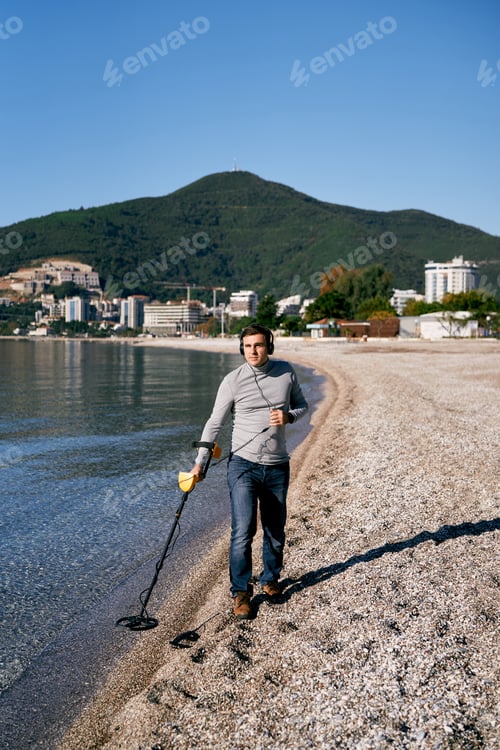 Preview: Beach cop runs a metal detector through the shallow sea, listening to headphones