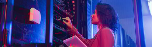 Preview: engineer holding digital tablet while checking server in data center in neon light, banner