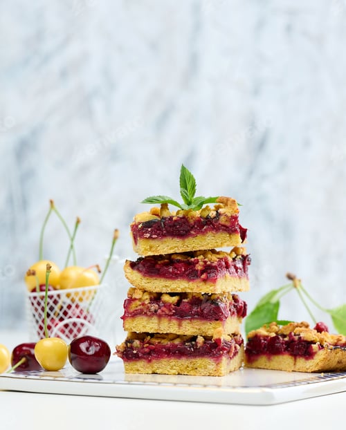 Preview: Square slices of cherry crumble lie in a stack on a white board
