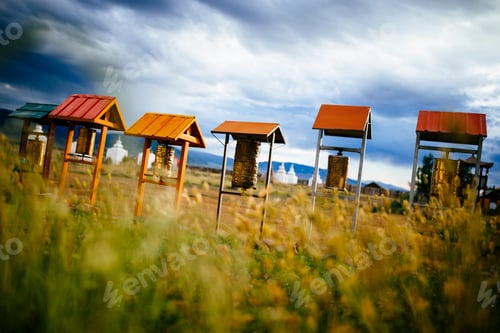 Preview: Buddhist prayer drums under small wooden roofs, monuments in the background.