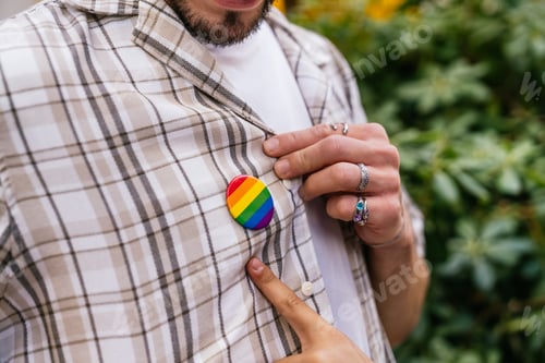 Preview: Person showing pride rainbow pin on plaid shirt