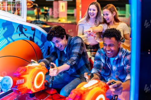 Preview: Happy multiethnic friends playing arcade games in an entertainment venue
