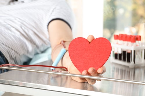 Preview: Man holding heart while making blood donation at hospital, closeup