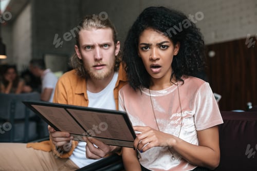Preview: Shocked African American girl and boy amazedly looking in camera at cafe