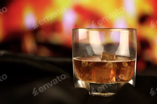 Preview: Whisky or whiskey or bourbon with ice on wooden surface on fireplace