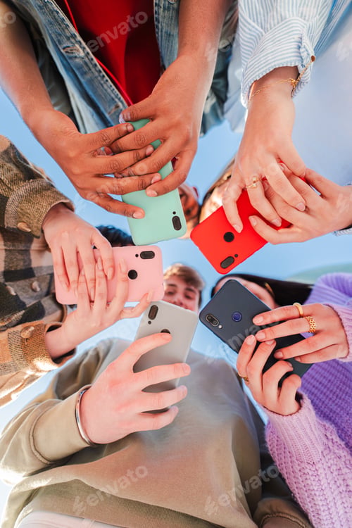 Preview: Vertical low angle view of a group of unrecognizable multiracial young friends using their