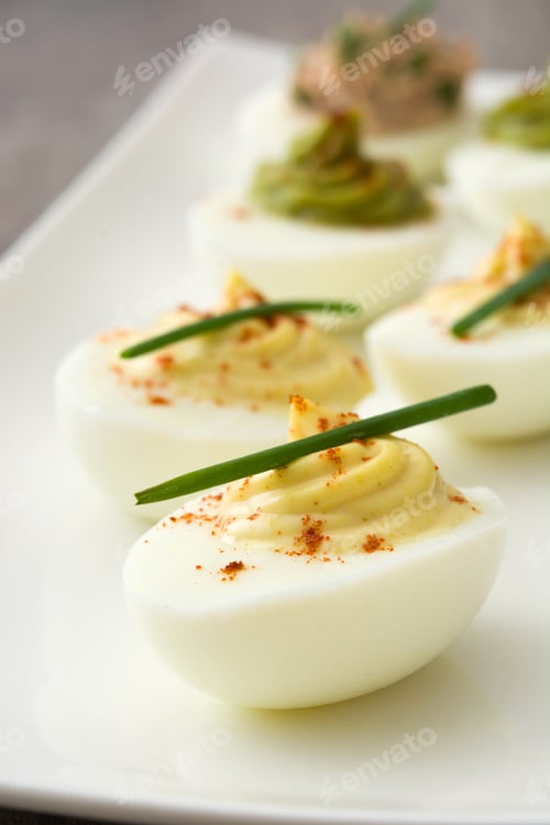 Preview: Deviled eggs garnished with paprika and chives resting on white rectangular plate