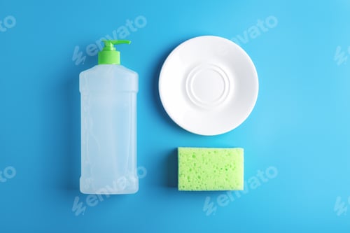 Preview: Kitchen flat lay with clean glass plate and dish washing supplies on blue background.