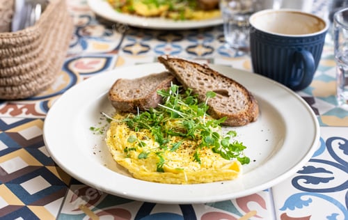 Preview: Omelette served with micro green and toasted bread on ceramic plate.