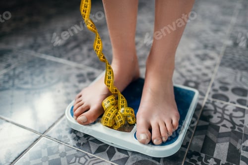 Preview: Female feet on the scales closeup, measuring tape