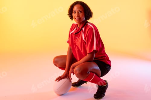 Preview: Portrait of happy african american female rugby player with rugby ball over neon yellow lighting