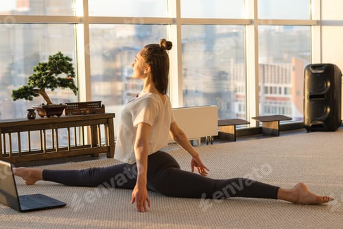 Preview: woman practicing yoga,Splits exercise in front of a laptop.Yoga and fitness online training concept