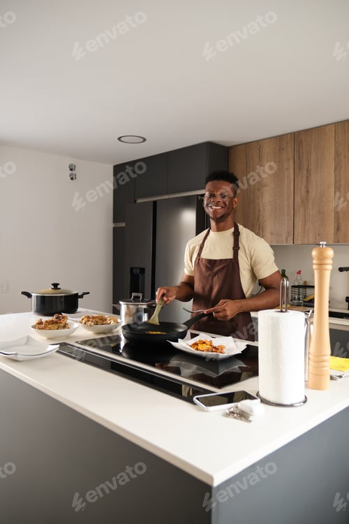 Preview: Young african man preparing fried chicken mince with vegetables and plantains.