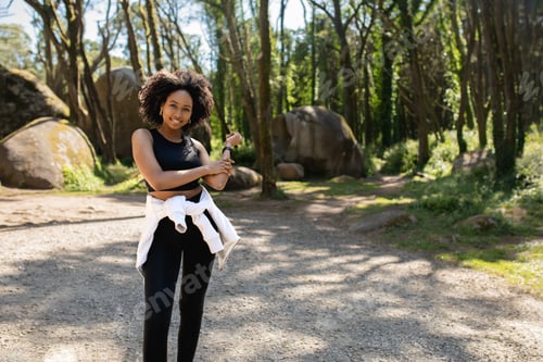 Preview: Happy black woman in sportswear resting while working out outdoors in the forest, smiling at camera