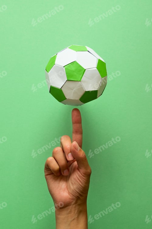 Preview: Hand spinning paper soccer ball on green background. Origami. Paper craft. Soccer game concept.