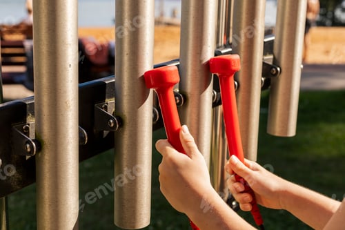 Preview: Children are playing an outdoor musical instrument featuring metal tubes. The sun shines brightly