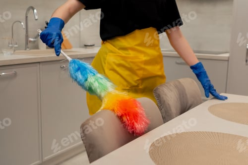 Preview: close up in the apartment cleaning lady in a yellow apron is cleaning chairs with a dust brush